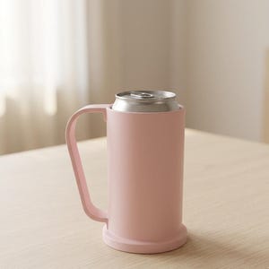 Puede incluir: Un enfriador de latas rosa claro con un asa, que contiene una lata de aluminio plateada. El enfriador tiene un cuerpo cilíndrico y una base. El asa es curva y está unida al lateral. La lata es visible en la parte superior.
