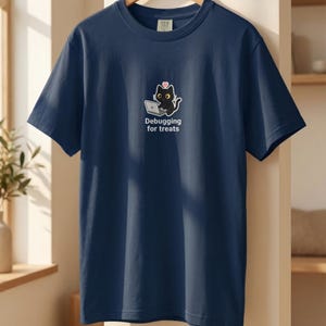 Peut inclure: T-shirt bleu marine avec un motif de chat noir utilisant un ordinateur portable, un cœur rose et le texte "Debugging for treats". Le t-shirt a des manches courtes et un col rond. Vêtement décontracté.