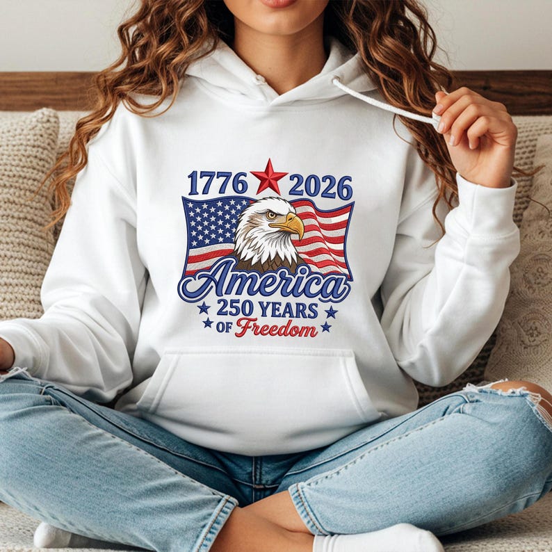 May include: White hoodie featuring a patriotic design. The graphic includes the text "1776 2026 America 250 Years of Freedom" with an American flag and an eagle. The design is in red, white, and blue.