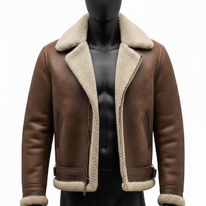 May include: Brown leather jacket with a cream-colored shearling lining and collar. The jacket features a zip closure, side pockets, and a buckled waist. The jacket is displayed on a black mannequin.