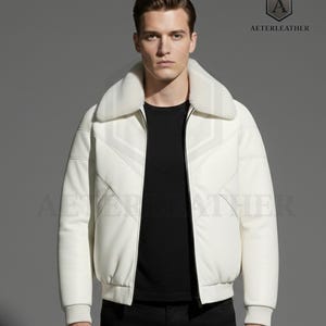 Könnte beinhalten: Weiße Lederjacke mit Pelzkragen. Die Jacke hat einen Reißverschluss vorne und gerippte Bündchen und Saum. Der Markenname "AETERLEATHER" ist in der oberen rechten Ecke sichtbar.
