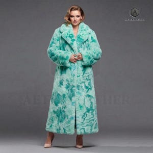 May include: A full-length, turquoise faux fur coat with a large collar and a subtle, abstract pattern in a darker shade of turquoise. The coat is worn by a person and has a button closure. The coat is a statement piece.