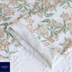 Puede incluir: Primer plano de tela blanca doblada con un estampado floral en tonos verdes y beige. La tela est&aacute; en capas, revelando una impresi&oacute;n detallada. El logotipo "OUT/IT RUSH" es visible en la esquina inferior izquierda.