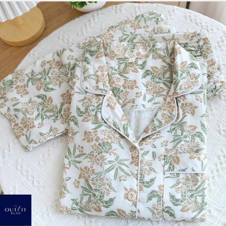 Puede incluir: Conjunto de pijama blanco con estampado floral en tonos verdes y beige. El conjunto incluye una camisa abotonada con bolsillo en el pecho y pantal&oacute;n a juego. Los pijamas son de tejido suave y est&aacute;n sobre una superficie blanca.