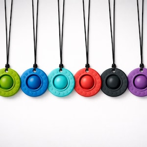 May include: Six brightly coloured pendant necklaces. Each necklace has a circular pendant with a central sphere and a textured outer ring. The pendants are green, blue, teal, red, black, and purple, suspended from black cords.