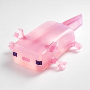 Peut inclure: Figurine d'axolotl rose translucide avec des traits carrés. Le jouet a de petites pattes, des branchies et une queue détaillées. Le visage de l'axolotl a des accents violets et roses, lui donnant une apparence mignonne. Le jouet est probablement un objet de collection ou décoratif.
