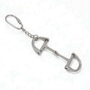 May include: A silver-coloured metal keyring featuring a horse bit design. The bit has a central joint and D-shaped rings on each end, connected to a chain and a keyring. The equestrian-themed accessory is shown against a white background.