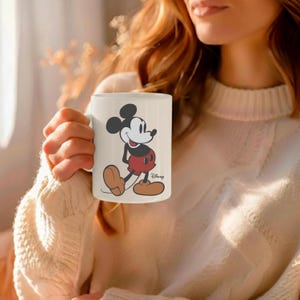 Pu&ograve; includere: Tazza in ceramica bianca con un classico design a cartoni animati di Topolino. L'illustrazione mostra Topolino con i suoi iconici pantaloncini rossi, scarpe gialle e guanti neri. Il logo Disney &egrave; stampato in basso a destra.