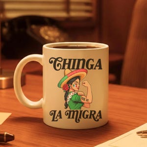 May include: White ceramic mug featuring a graphic of a woman in a sombrero flexing her arm, with the words "Chinga La Migra" in black script. The woman has a rose in her hair and a tattoo that says "Fuck ICE".