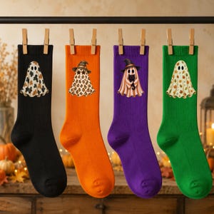 May include: Four pairs of ribbed crew socks in black, orange, purple, and green. Each sock features a unique ghost graphic: a cow-print ghost, a leopard-print ghost wearing a witch hat, a ghost holding a black cat, and a ghost with autumn leaves.