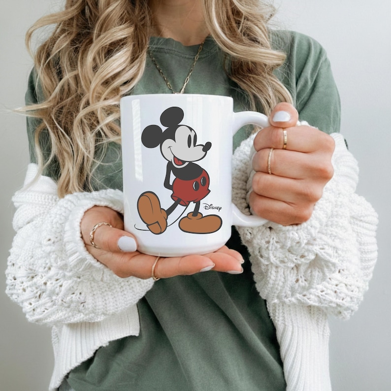 Pu&ograve; includere: Tazza in ceramica bianca con un'illustrazione a figura intera di Topolino nel suo abito classico. Il design include le orecchie nere, i pantaloncini rossi e le scarpe marroni di Topolino. Il logo Disney &egrave; stampato sotto.