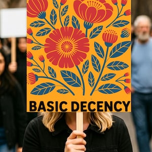 Pode incluir: Uma placa de protesto com o texto "RADICALIZED BY BASIC DECENCY" em um fundo amarelo. A placa apresenta um design floral em vermelho e azul, segurada por uma pessoa.