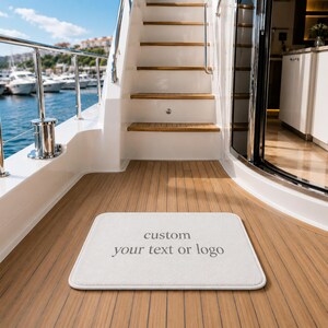May include: A rectangular white floor mat with rounded corners featuring the gray text custom your text or logo centered on the surface. The mat is positioned on a wooden deck of a boat with white stairs and a metal railing visible in the background.