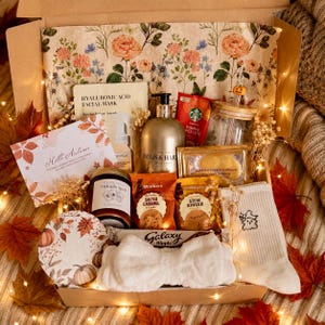 May include: A gift box containing a Hyaluronic Acid facial mask, a Baylis & Harding bottle, a Starbucks Pumpkin Spice Latte packet, a glass tumbler with a lid, a Midnight Spell candle, Walkers biscuits, a Galaxy Ripple bar, and white socks.