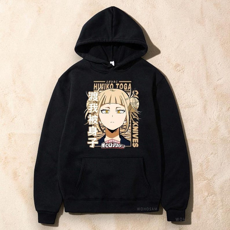 May include: A black hooded sweatshirt featuring a graphic print of the anime character Himiko Toga. The design includes the text Himiko Toga, Knives, and Japanese characters in a tan color palette, along with a small logo at the bottom center.