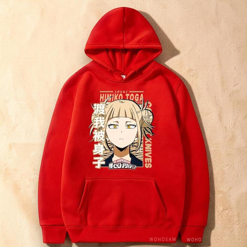 May include: A bright red hooded sweatshirt featuring a graphic print of the anime character Himiko Toga with blonde hair and yellow eyes. The design includes the text Himiko Toga, Knives, and Japanese characters, along with the My Hero Academia logo.