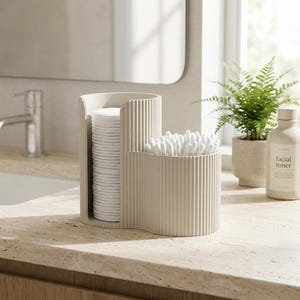 May include: A beige, ribbed, two-compartment organiser for bathroom essentials. One section holds a stack of white cotton pads, the other is filled with cotton buds. The organiser sits on a light-coloured countertop.