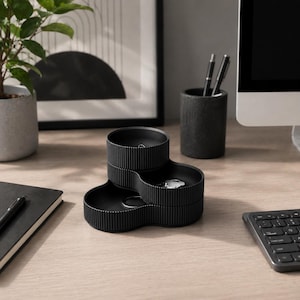 May include: A black desk organiser with three tiered sections. The organiser has a ribbed texture and holds a set of keys. A pen holder and a notebook are also on the desk.