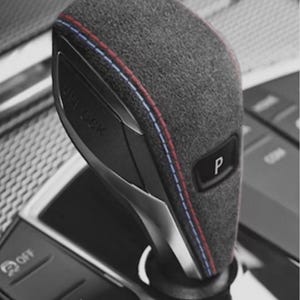 May include: A close-up of a car gear shift lever. The lever is grey with red and blue stitching. The lever has a button marked "P". Other buttons include "OFF", "START ENGINE STOP", and "SPORT".