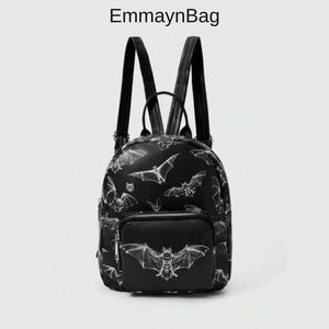 May include: A black backpack featuring a white line-art bat pattern and the text EmmaynBag at the top. The bag includes a front zipped pocket with a large bat graphic, two adjustable shoulder straps, and a top handle for carrying convenience.