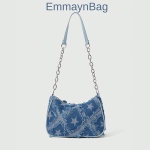 Peut inclure: Un sac à bandoulière en jean avec une sangle bleu clair et une chaîne argentée. Le sac présente un motif patchwork avec des étoiles. Le texte "EmmaynBag" est en haut de l'image.