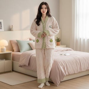 May include: A light pink pajama set with a cable knit design. The set includes a button-up jacket with green trim and two pockets with green shamrock appliques. The matching pants have green trim at the ankles. The word "Love" is embroidered on the jacket.