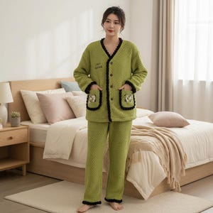 May include: A green quilted pajama set. The jacket has a V-neck, black trim, and pockets with floral embroidery. The pajama set includes a button-down jacket and matching trousers. The text "dream" is embroidered on the jacket.