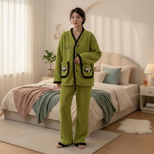 May include: Green textured pajama set featuring a jacket with black trim, panda pocket details, and a V-neck. The matching trousers have black trim at the ankles. The button-down set is designed for comfort and warmth, perfect for lounging.