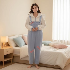 May include: A light blue and white hooded jumpsuit with pink bow accents. The jumpsuit features a zip-up front, light blue overalls, and a white hooded top. The outfit is made of a soft, plush material, perfect for lounging or sleepwear.