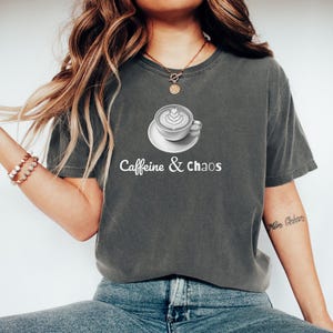 May include: Dark grey t-shirt with the text "Caffeine & chaos" and a graphic of a coffee cup with latte art. The shirt is a relaxed fit and has short sleeves.