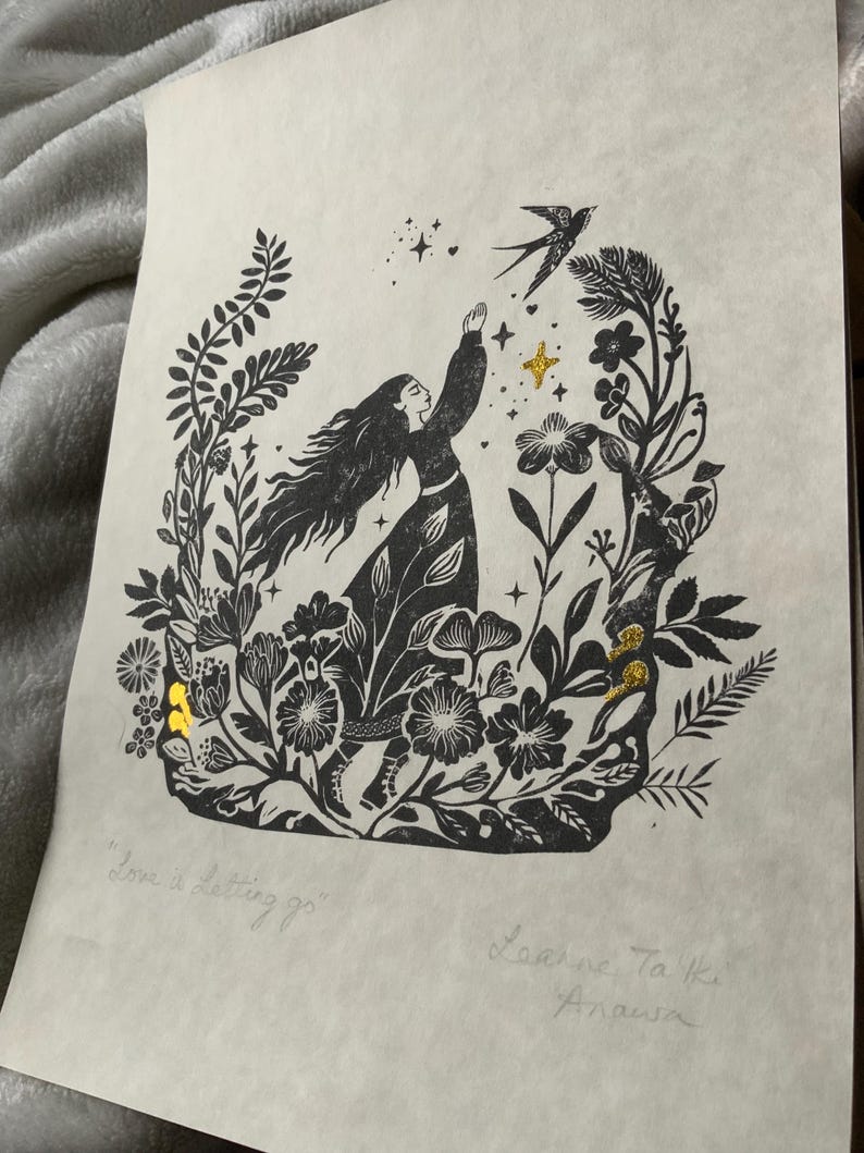 May include: Black and white linocut print of a woman reaching for a bird, surrounded by flowers and foliage. The print has gold foil accents and the text "Love is Letting go". Signed by the artist.