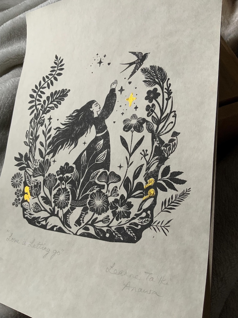 May include: Black and white art print featuring a woman reaching for a bird, surrounded by floral elements. Gold accents highlight stars and details. The text "Love is letting go" is visible, along with the artist's signature.