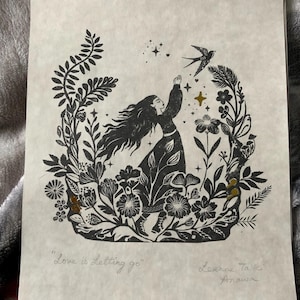 May include: Black and white linocut print featuring a woman reaching for a bird, surrounded by floral elements. The print includes the text "Love is Letting go" and artist's signature. The artwork has a vintage aesthetic.