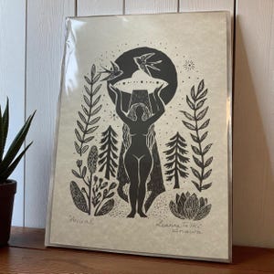 May include: Black and white art print featuring a silhouetted figure holding a circular object with two birds above. The print includes botanical elements and the word "Arrival". Signed by the artist, Leanne Ta'ike Anawa.