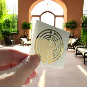 Könnte beinhalten: Ein weißer Aufkleber mit einem goldenen Spiralmuster und dem aufgedruckten Text "SPIRIT OF LEMURIA".