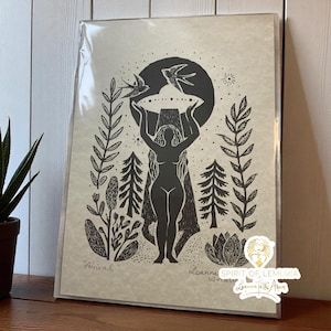 May include: Black and white art print featuring a silhouetted figure holding a circular object with two birds above. The print includes botanical elements and the word "Arrival". The artwork is in a protective sleeve.