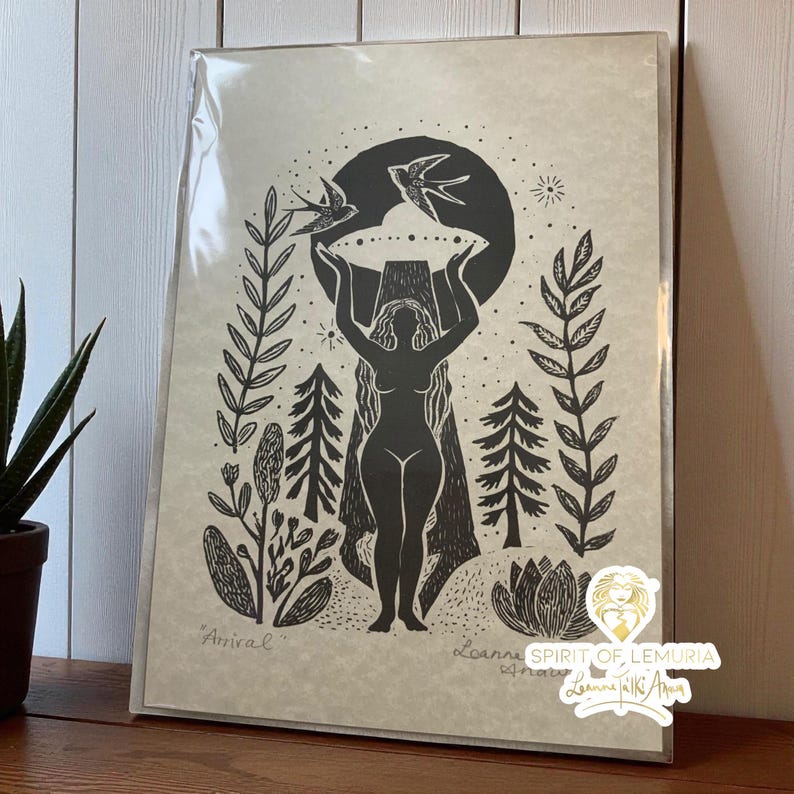 May include: Black and white art print featuring a silhouetted figure holding a circular object with two birds above. The print includes botanical elements and the word "Arrival". The artwork is in a protective sleeve.