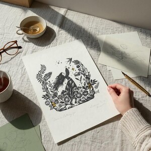 May include: Black and white art print featuring a woman surrounded by flowers and a bird. The print includes the text "Love is letting go". A cup of tea, glasses, and a pen are also visible.