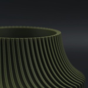 May include: An olive green cylindrical vessel featuring a series of vertical, raised ridges that extend from the top rim down to the base, creating a textured, ribbed surface pattern across the exterior of the object against a dark background.