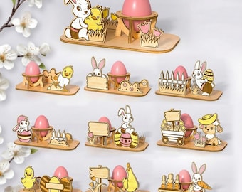 May include: A collection of Easter-themed wooden decorations. Each decoration features a pink egg, a bunny, and other Easter-related elements like chicks, flowers, and signs. The decorations are on a light-colored wooden base.