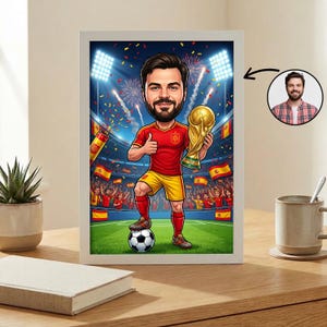 以下が含まれることがあります： 赤と黄色のサッカーユニフォームを着た髭のある人物がサッカーボールの上に立ち、スタジアムで金色のトロフィーを掲げている様子を描いた額入りカリカチュア。小さな円形のインセットには、同じ人物の写真が表示されています。