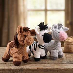 May include: Three crocheted animal figures: a brown horse, a zebra with black stripes, and a gray donkey with a pink nose. The handmade toys are displayed on a wooden surface, with a burlap sack of grains in the background.