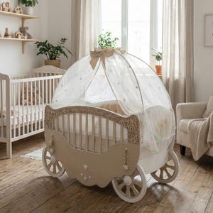 Può includere: Una culla beige e bianca in stile carrozza con intagli decorativi e ruote. La culla è dotata di un baldacchino con dettagli a forma di stella e un grande fiocco. Sullo sfondo è visibile una seconda culla, insieme a mensole e piante.