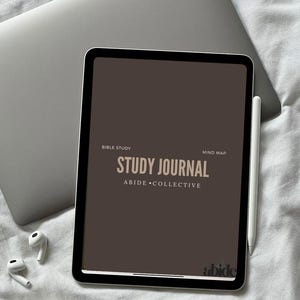May include: A digital tablet displaying a "Study Journal" with the text "Abide Collective." The tablet is on a white surface, next to a laptop, wireless earbuds, and a stylus. The journal's color is a muted brown.