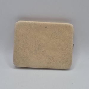 May include: A rectangular, off-white compact case with a textured, cross-hatched surface finish. The object features rounded corners and a slim profile, presenting a uniform, light-colored exterior with subtle signs of wear on the front face.