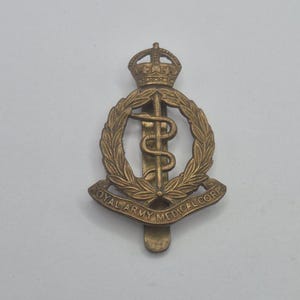 May include: A brass Royal Army Medical Corps badge. The badge features a crown, a staff with a snake, and a laurel wreath. The text "ROYAL ARMY MEDICAL CORPS" is inscribed on the badge.
