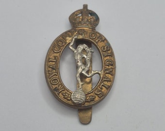 Op de afbeelding: Een badge van messing- en zilverkleurig metaal met het embleem van het Royal Corps of Signals. Het ontwerp bevat een centrale figuur van Mercurius die op een wereldbol staat, omringd door een ovaal kader met de tekst ROYAL CORPS OF SIGNALS.
