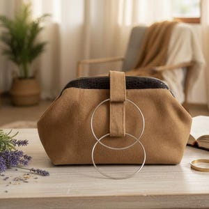Handbag pouch (clutch style) with silver rings. It is lightweight, made of camel-brown suede with a faux leather detail on the closure.