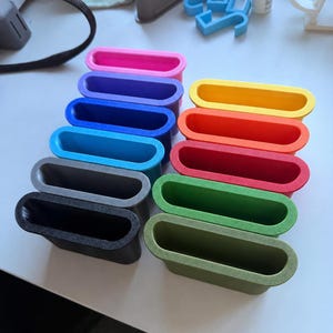 Puede incluir: Una colección de diez recipientes rectangulares abiertos en la parte superior, dispuestos en dos columnas. Los recipientes presentan un acabado liso y de color sólido en tonos rosa, morado, azul, azul claro, gris, negro, amarillo, naranja, rojo, verde y oliva.