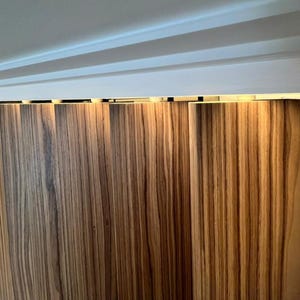 May include: Vertical wooden panels with a natural wood grain pattern. The panels are a warm brown color and appear to be part of a wall or partition. The image is well-lit, highlighting the texture of the wood.